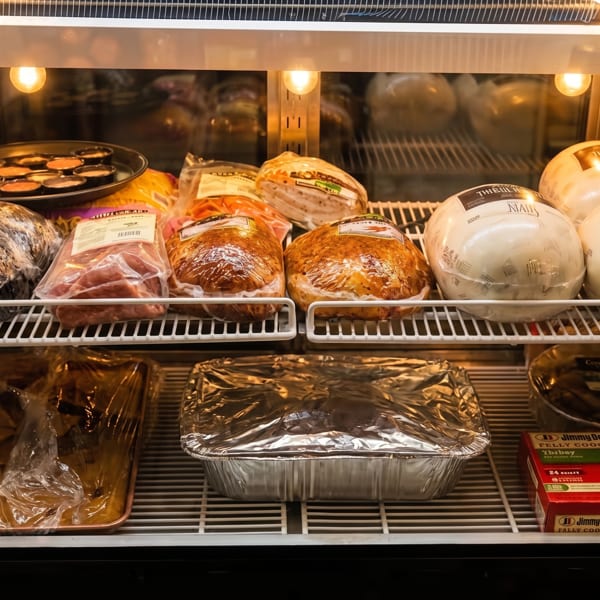 A refrigerated display case filled with packaged meats, including hams, and foil-covered trays.